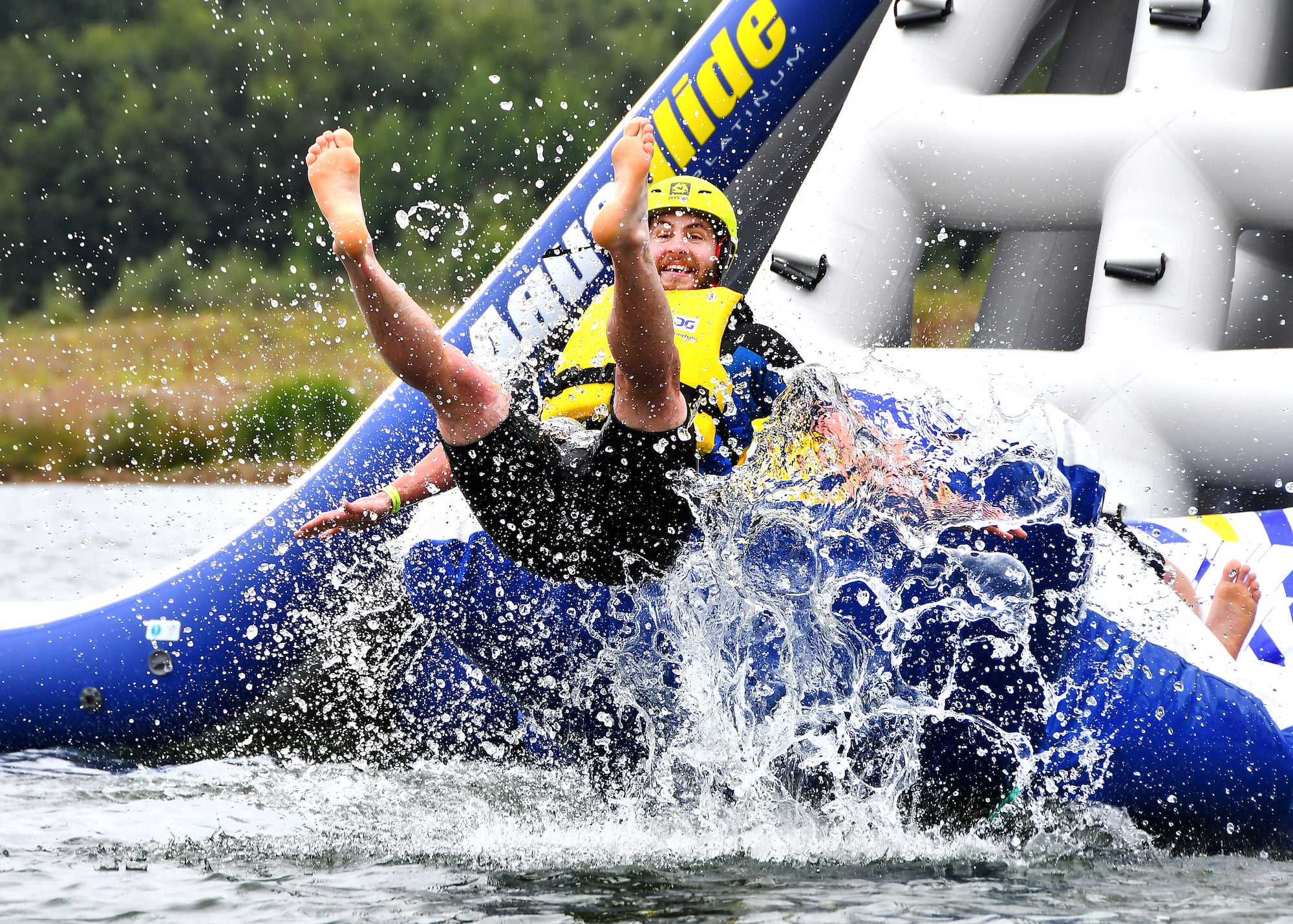 A man flies off the end of an inflatable slide, water splashed around him