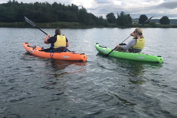 Two people wearing life jackets kayaking across a lake in North Yorkshire surrounded by greenery