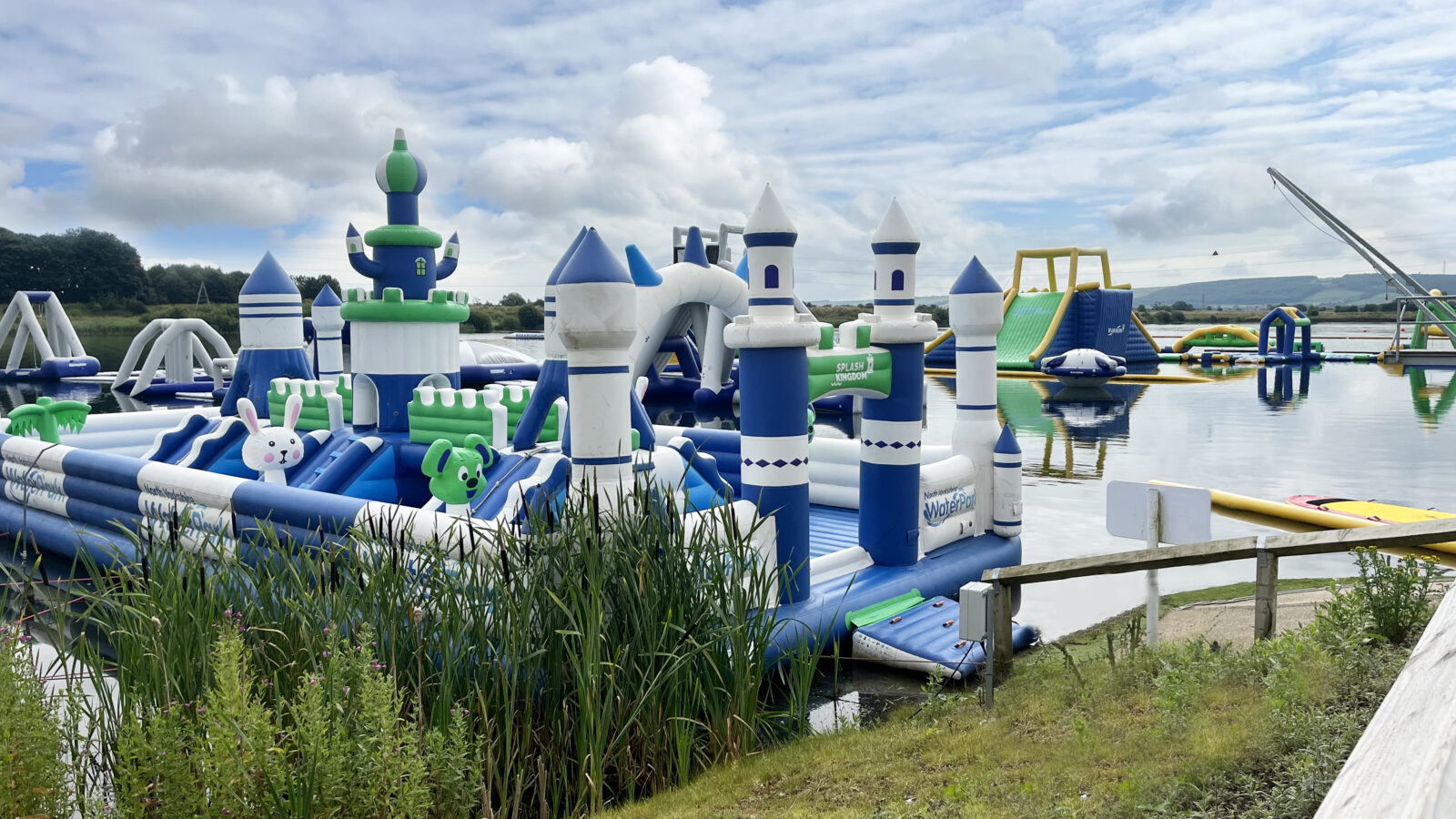 An inflatable castle AquaPark on a lake surrounded by greenery with other water park activities
