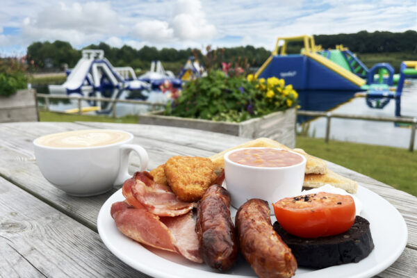 A full English breakfast with a cup of coffee on a table outdoors overlooking the North Yorkshire Water Park AquaPark