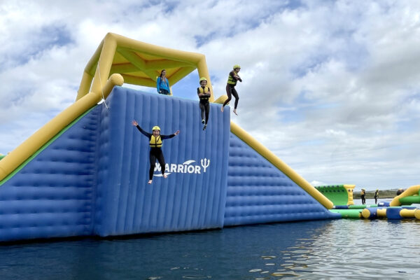 Three people excited and happy jumping from the top of an inflatable AquaPark activity into calm waters