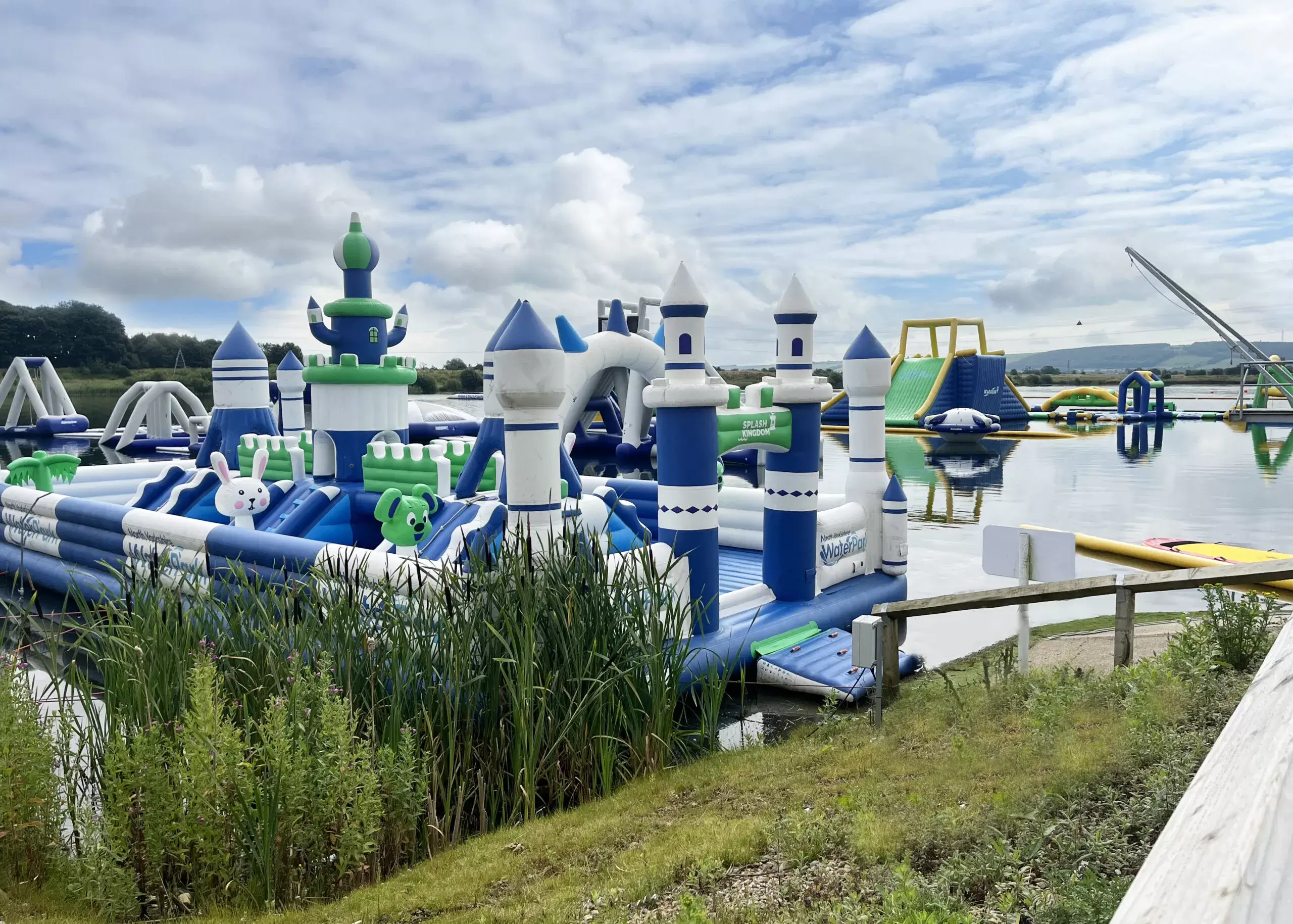 An inflatable castle AquaPark on a lake surrounded by greenery with other water park activities