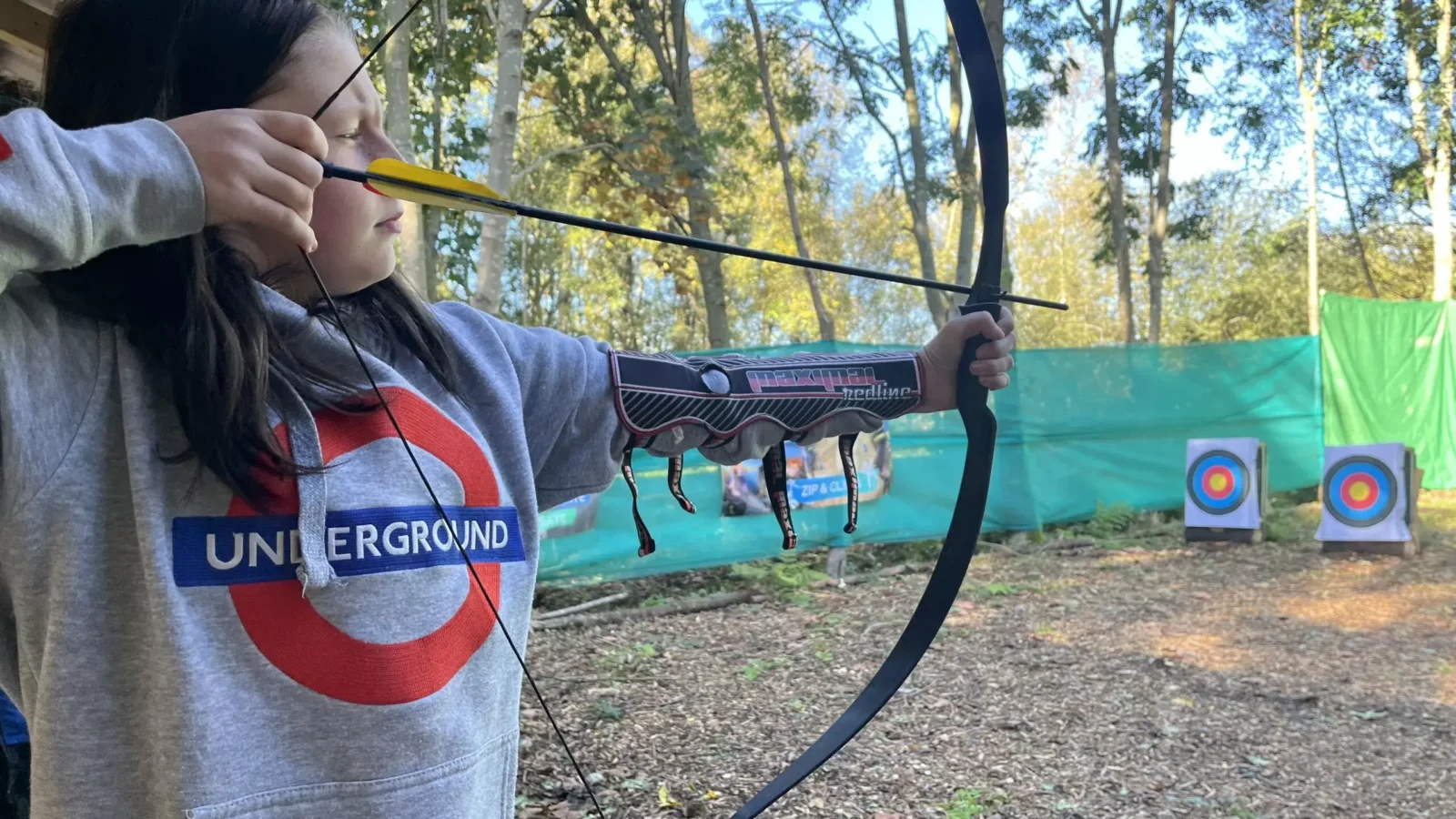 A young person prepares to fire an arrow at a brightly coloured target in a woodland in North Yorkshire