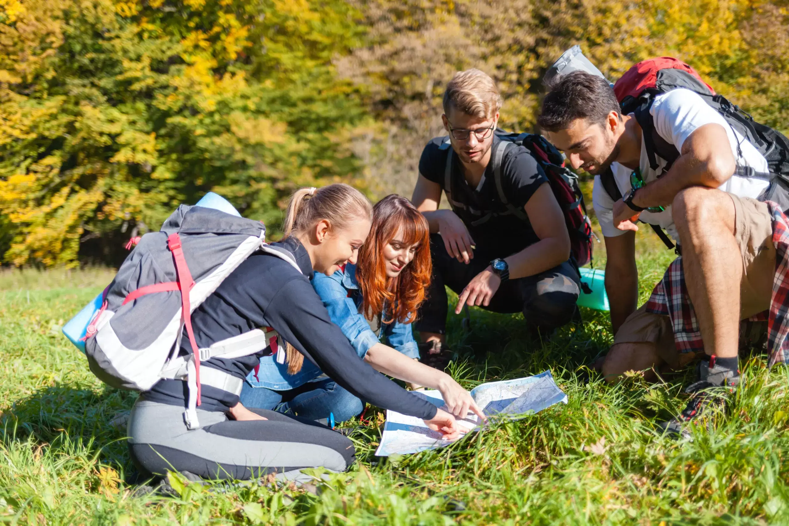 A group of smiling people wearing walking attire, knelt on the ground around a map on a sunny day in North Yorkshire