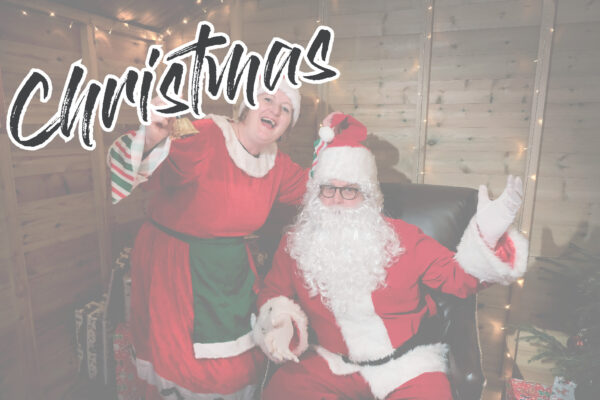 Mr and Mrs Clause Waving in a wooden grotto with the word Christmas on the picture